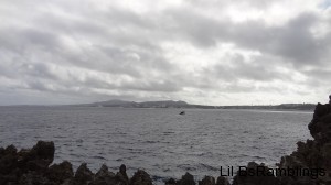 A view over rocks to a long bay with a city beyond