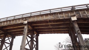 A view looking up of the wooden walkway supported by a woden arch.