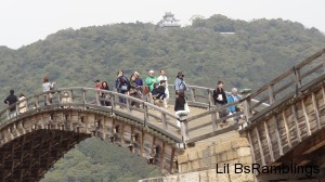 An arch of the wooden bridge under the distant Japanese castle on a mountaintop above.