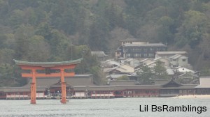 A large red Torii gate in front of a sprawling Japanese shrine