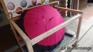 A pink cloth umbrella with black edging under a constant trickle of water.
