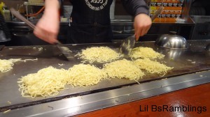 A cook using two spatulas to toss a set of noodles like one would mix a salad.