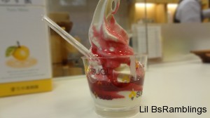 A cup of ice cream squeezed out of it's machine driping with dark red berry sauce