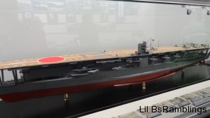 Two model ships, one an aircraft carrier, behind glass.