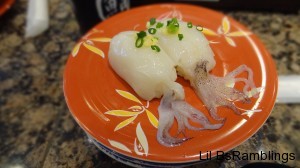 Two pieces of white octopus with the tentacles spreadover rice on an orange plate