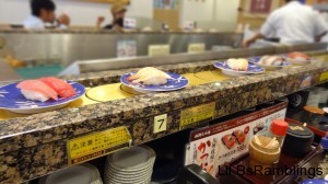 Plates of raw fish over a square of rice, two pieces on a plate, circle the table around the chef creating the pieces