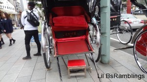 A red and silver two seat carriage pulled by a man.