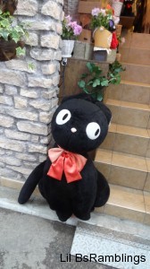 A large stuffed black cat similar to the one in Kiki's Delivery Service leans on a wall next to stairs