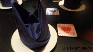 A folded blue cloth napkin on a plate and blue or pink coasters at each  place.