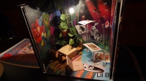 A box of paper art showing a garden party with playing cards on pillars nearby.