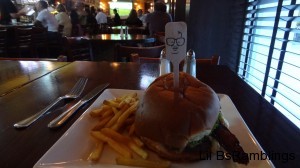 A burger and fries in a bar with a stick in the burger.  The stick has a face on it.